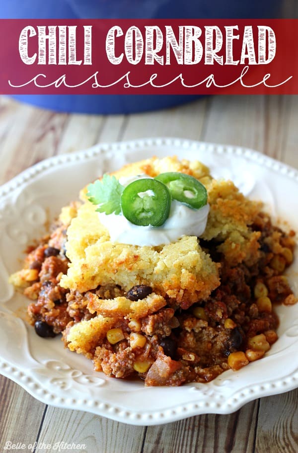 a plate of chili with cornbread, sour cream, and sliced jalapeño on top