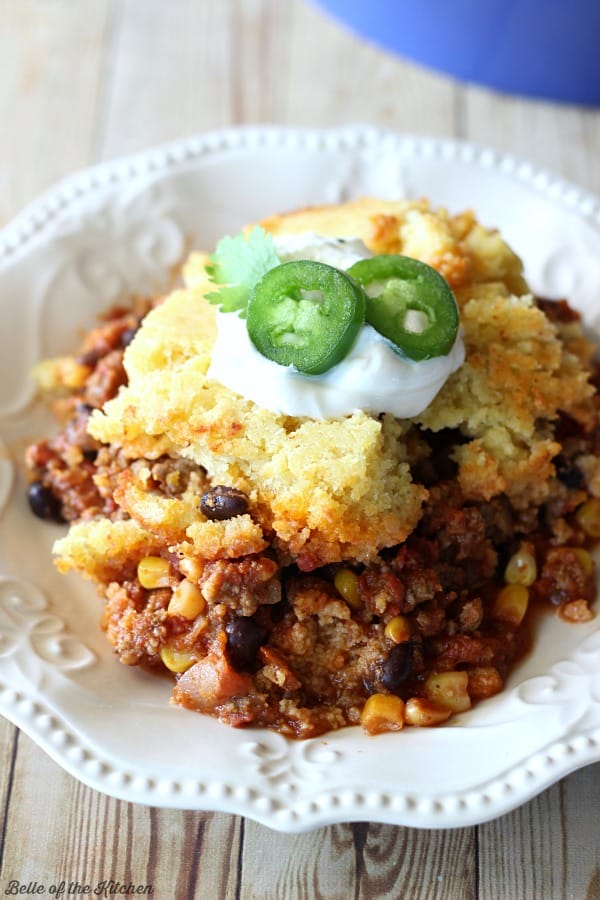 a plate of chili with cornbread, sour cream, and sliced jalapeño on top