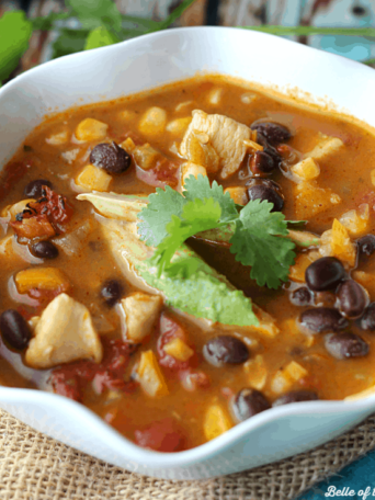 A bowl of chicken taco soup with a sprig of cilantro and avocado