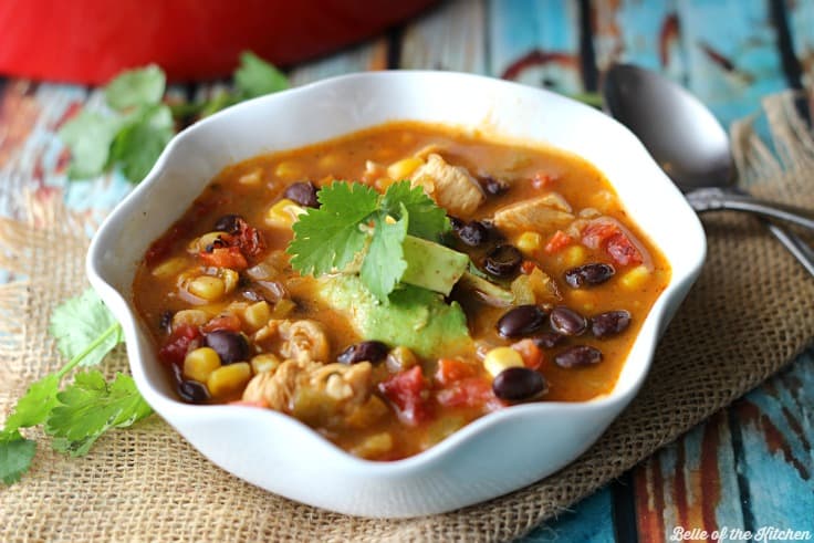 A bowl of chicken taco soup with a sprig of cilantro and avocado