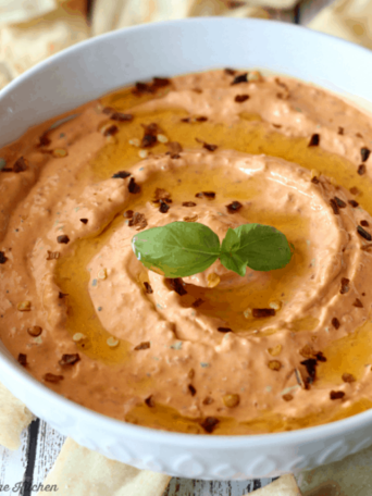 A bowl of red pepper dip surrounded by pita chips