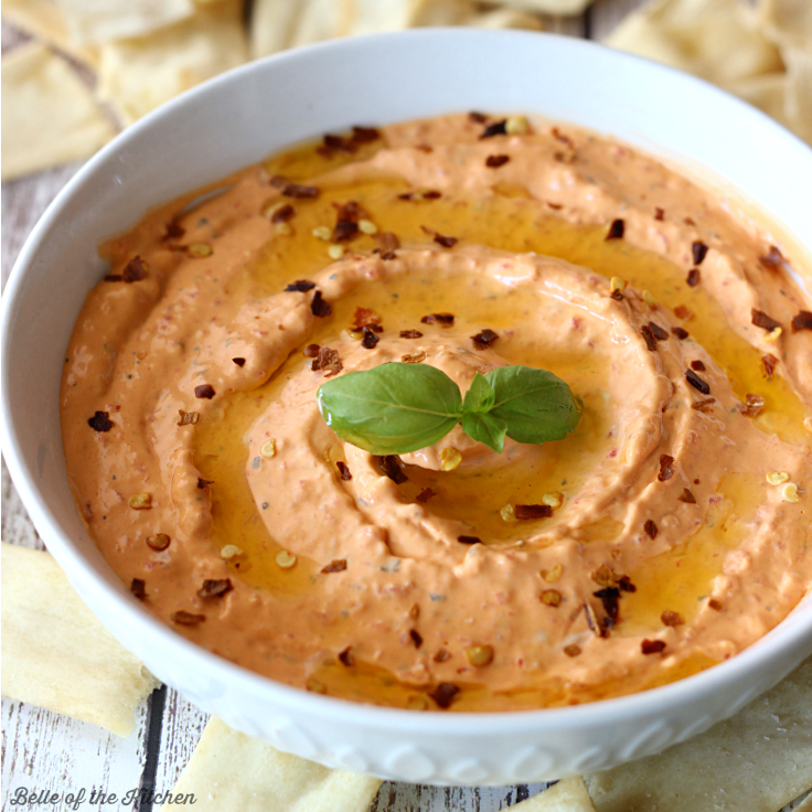 A bowl of red pepper dip surrounded by pita chips