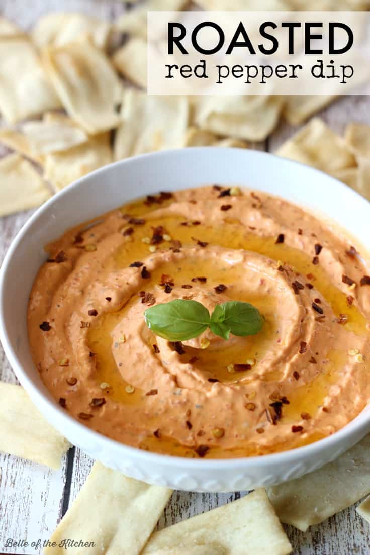 A bowl of red pepper dip surrounded by pita chips