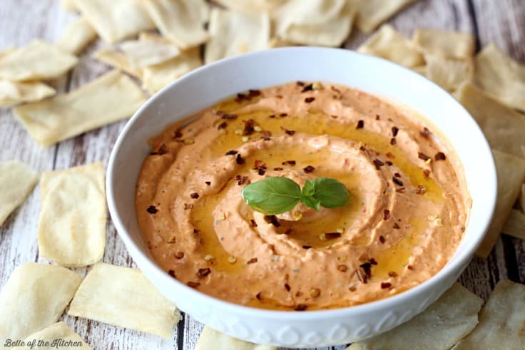 A bowl of red pepper dip surrounded by pita chips