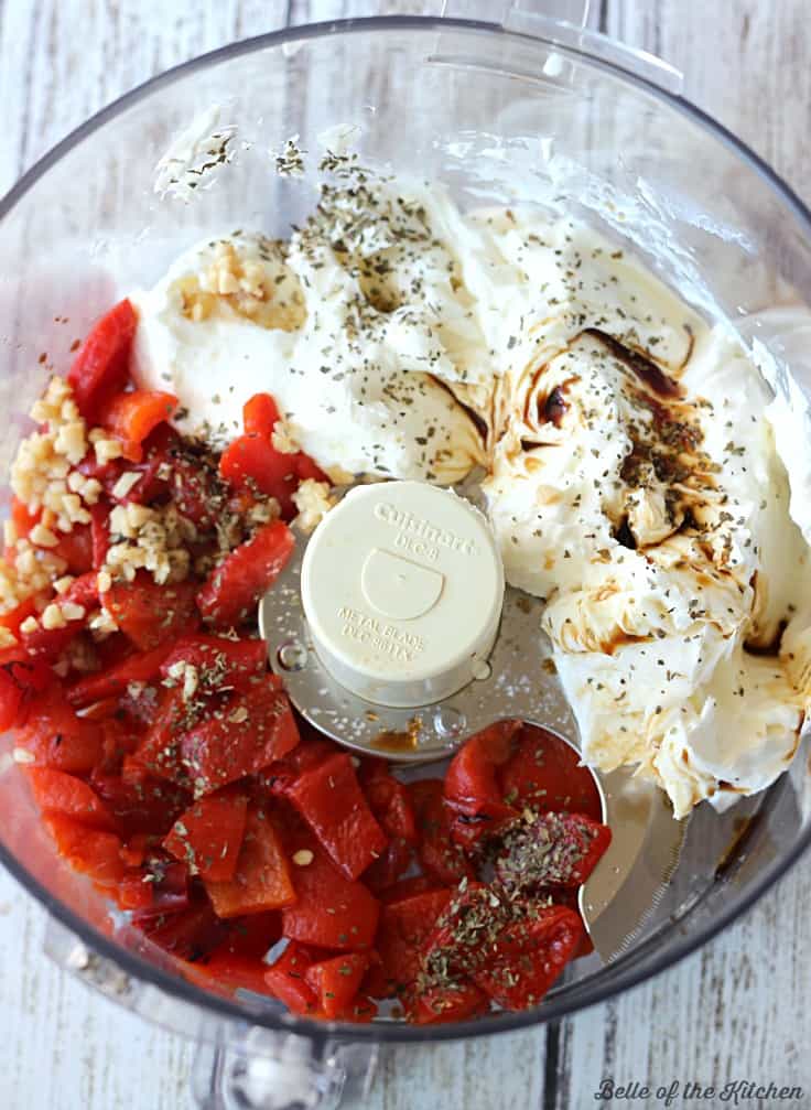a food processor bowl filled with roasted red peppers, garlic, and cream cheese