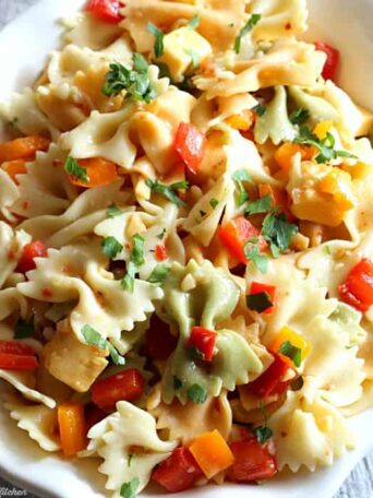 A close up of a bowl of pasta salad with cheese and chopped peppers