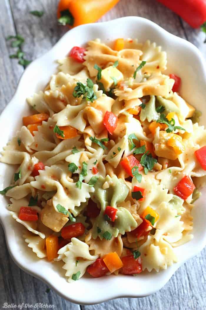 A close up of a bowl of pasta salad with cheese and chopped peppers