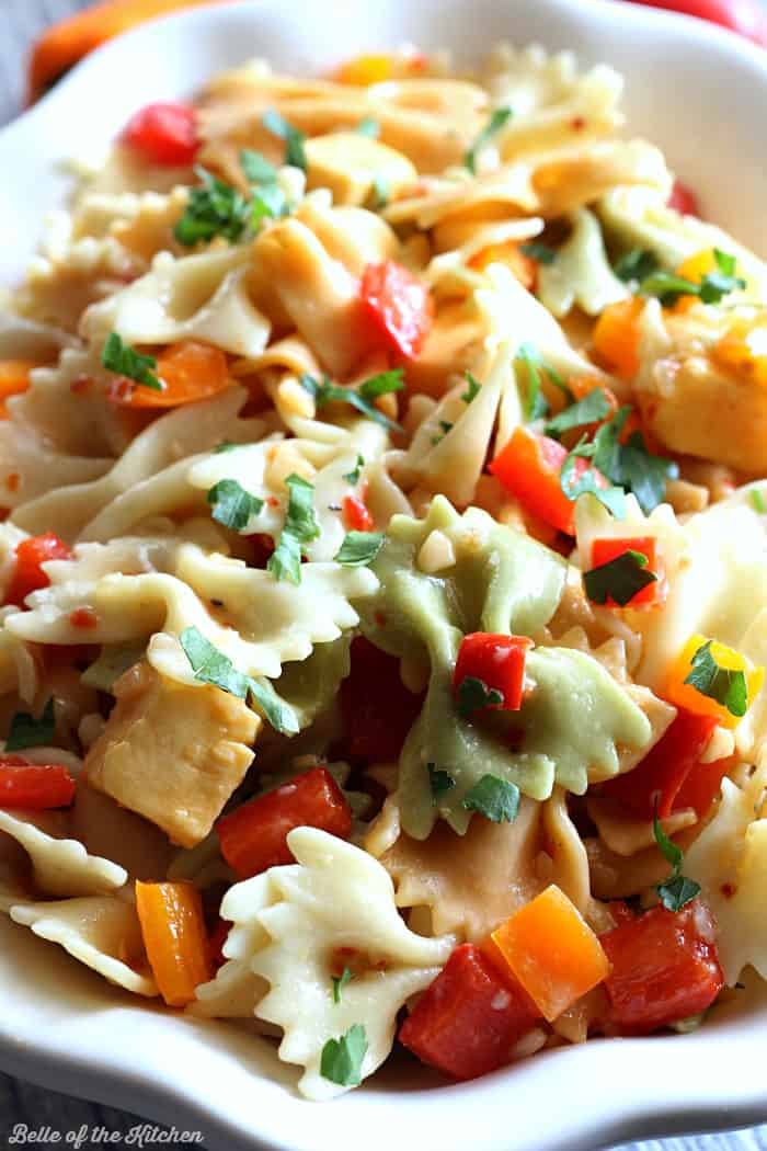 A close up of a bowl of pasta salad with cheese and chopped peppers