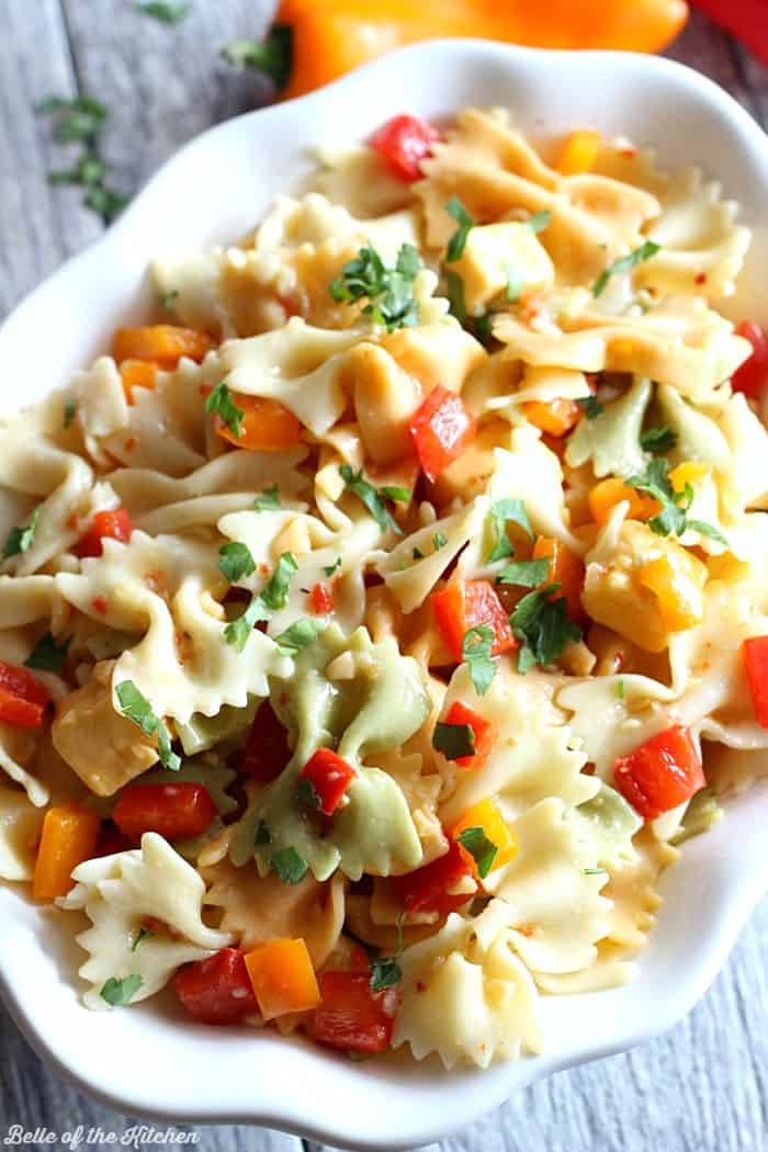 A dish is filled with bow tie pasta, cheese, and chopped red pepper