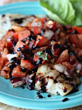 A blue plate topped with tilapia and bruschetta