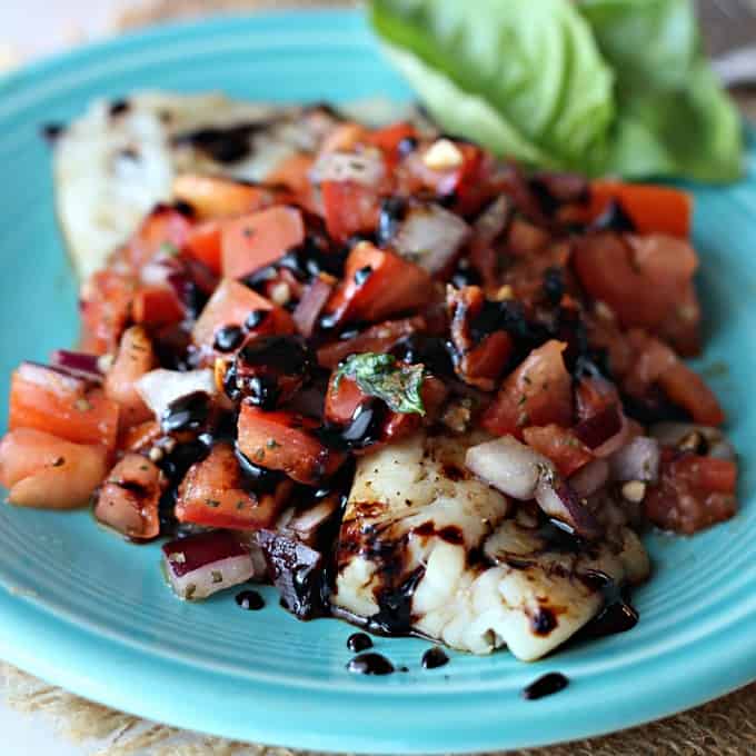 A blue plate topped with tilapia and bruschetta