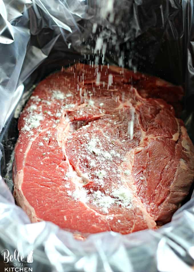 A close up of a chuck roast in a crockpot being sprinkled with seasoning