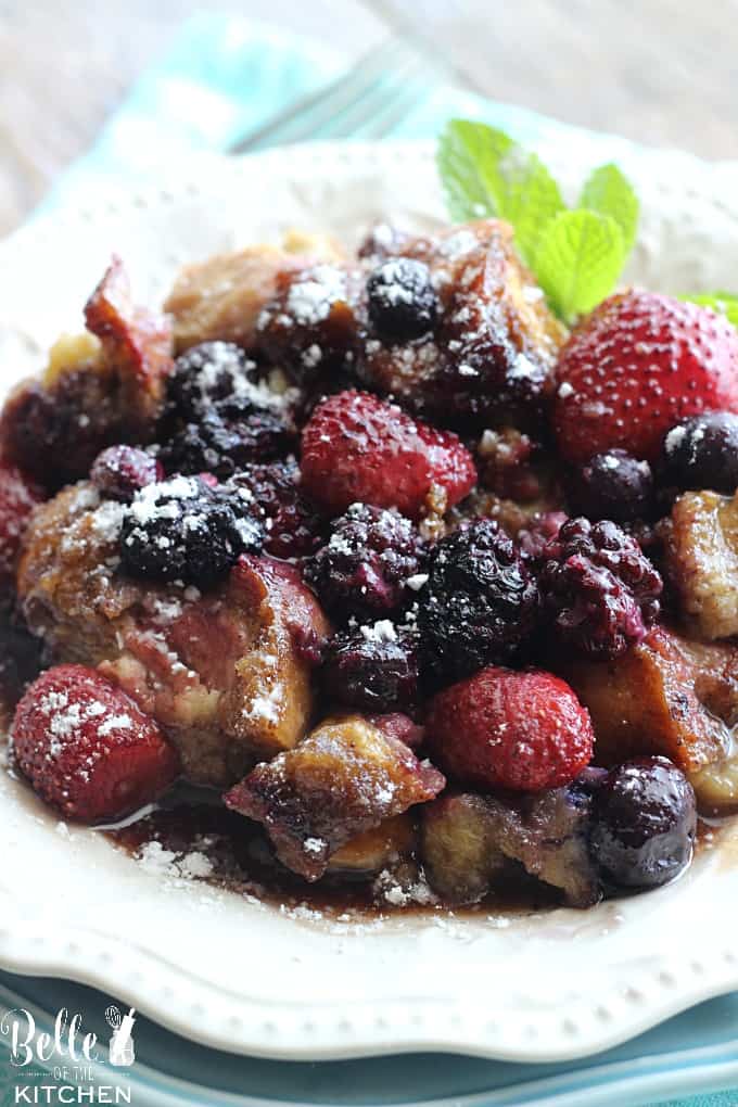 A plate of French toast casserole with berries on top and a sprig of mint on the side