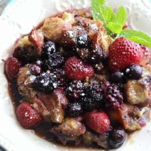 A plate of French toast casserole with berries on top and a sprig of mint on the side