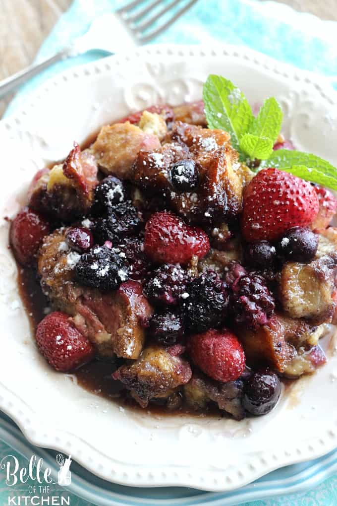 A plate of French toast casserole with berries on top and a sprig of mint on the side 