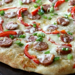 This Cajun Sausage Pizza starts with your favorite pizza dough, then gets piled with a creamy homemade sauce, andouille sausage, peppers, and gooey cheese.