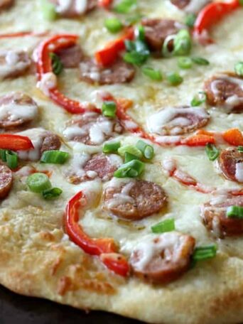 A pizza covered in cheese, sausage, peppers, and green onions