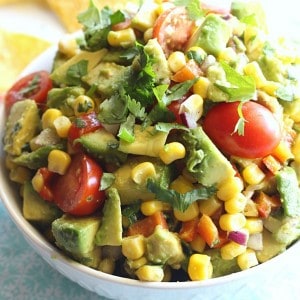 A dish filled with corn and avocado salsa with tomatoes and cilantro