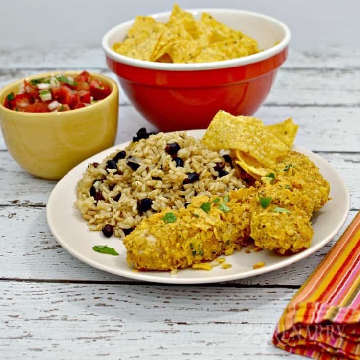 A plate of chicken tenders with rice and beans with a bowl of pico and tortilla chips