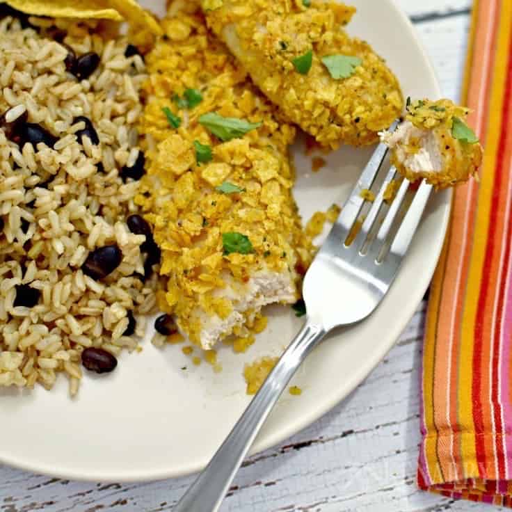 A plate of chicken tenders with rice and beans with a fork