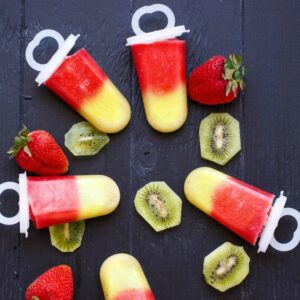 popsicles on a table surrounded by strawberries and sliced kiwi