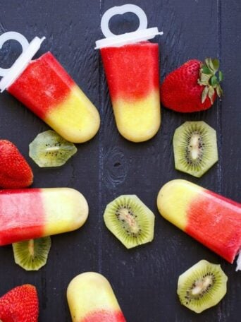 popsicles on a table surrounded by strawberries and sliced kiwi