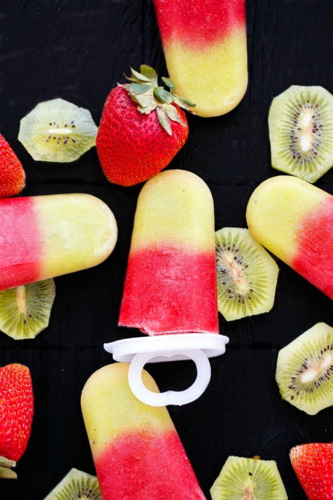 popsicles on a table surrounded by strawberries and sliced kiwi