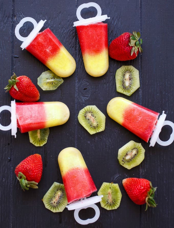 popsicles on a table surrounded by strawberries and sliced kiwi