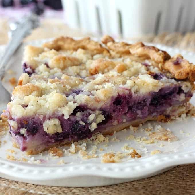 A close up of a piece of pie on a plate, with blueberries