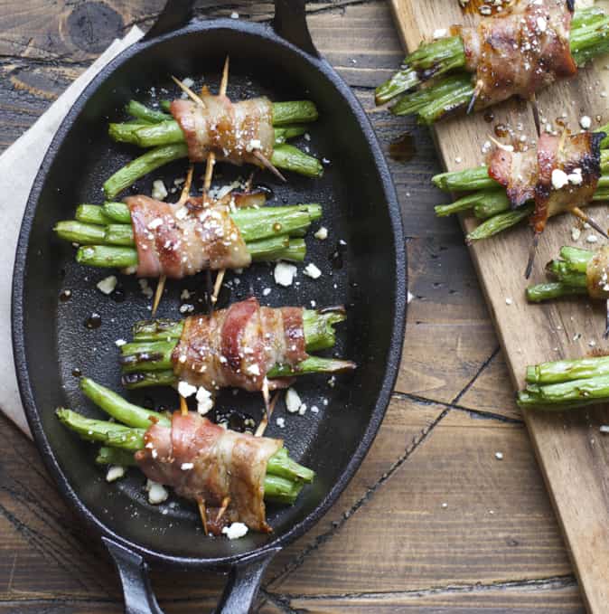 A close up of food on a wooden table, with Bacon and green beans bundles