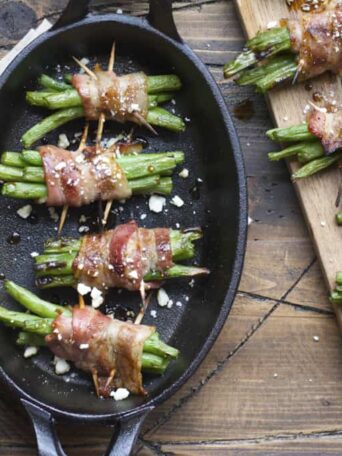 A close up of food on a wooden table, with Bacon and green beans bundles
