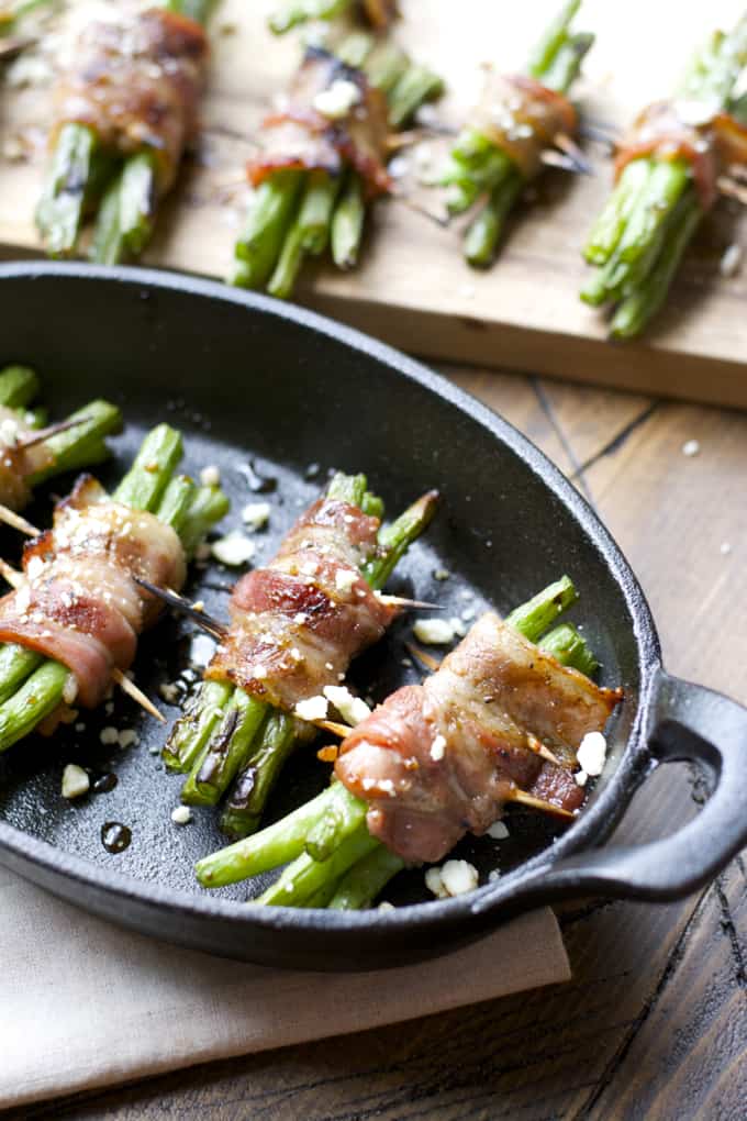 A close up of food on a wooden table, with Bacon and green beans bundles