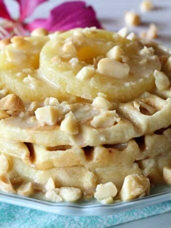 A close up of a plate of waffles with macadamia nuts and pineapple with a flower in the background