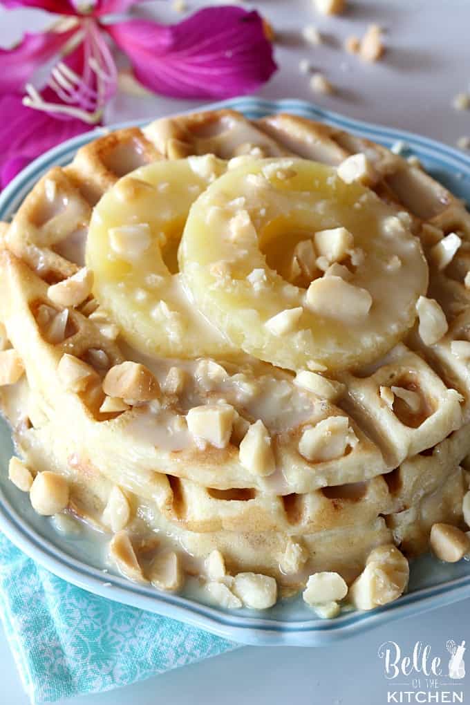 A close up of a plate of waffles with macadamia nuts and pineapple with a flower in the background