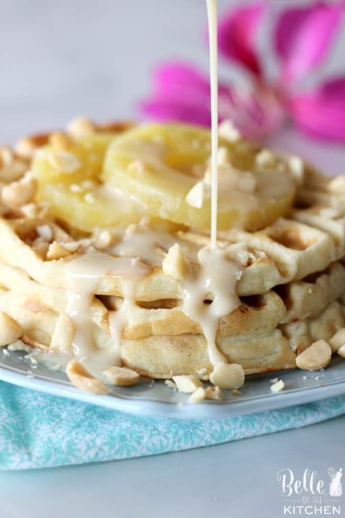 A close up of a plate of waffles with macadamia nuts and pineapple being drizzled with syrup