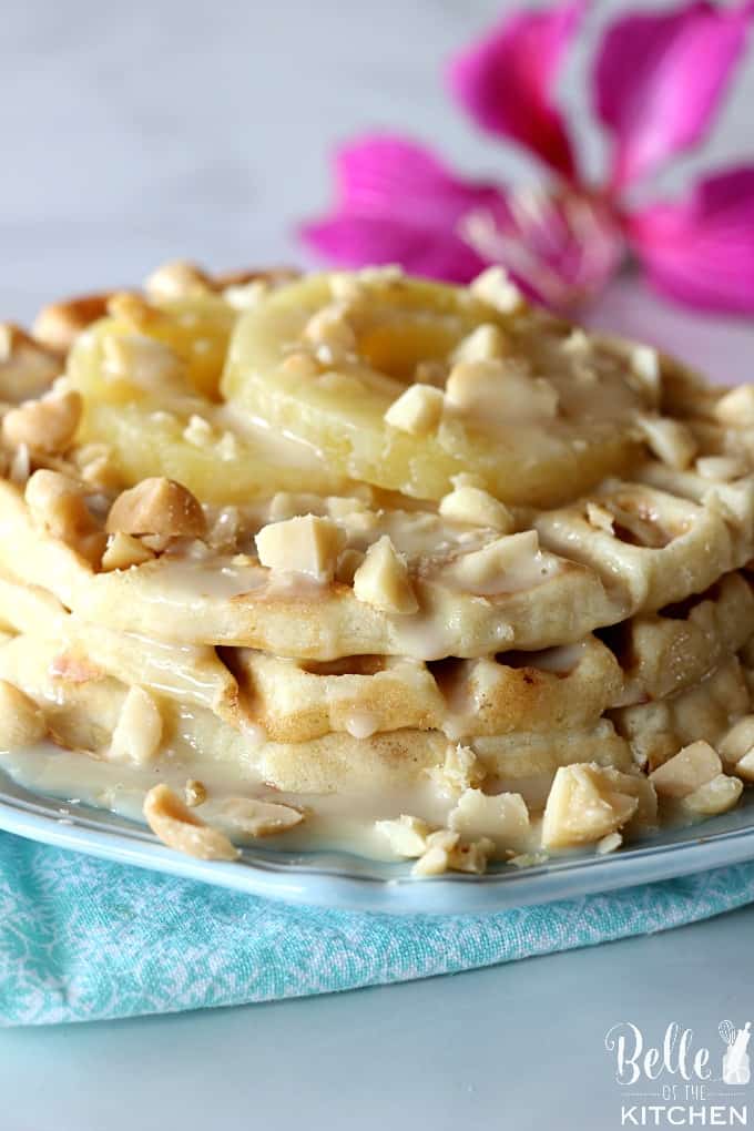 A close up of a plate of waffles with macadamia nuts and pineapple with a flower in the background