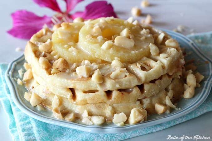A close up of a plate of waffles with macadamia nuts and pineapple with a flower in the background