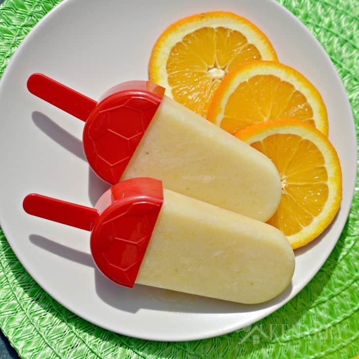 two Popsicles on a plate with sliced oranges