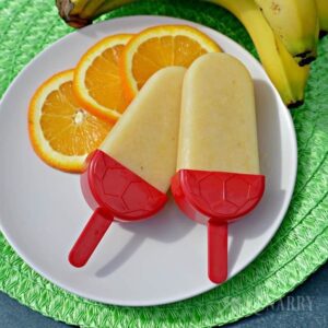 two Popsicles on a plate with sliced oranges and bananas