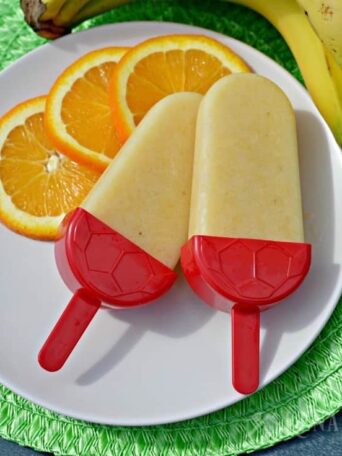 two Popsicles on a plate with sliced oranges and bananas