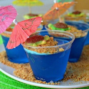 blue jello cups on a plate with graham cracker crumbs, topped with mini umbrellas