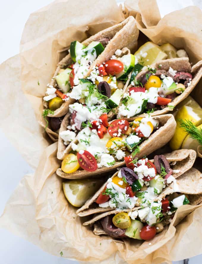 A bowl filled with Pitas and Steak, tomatoes, and lemons
