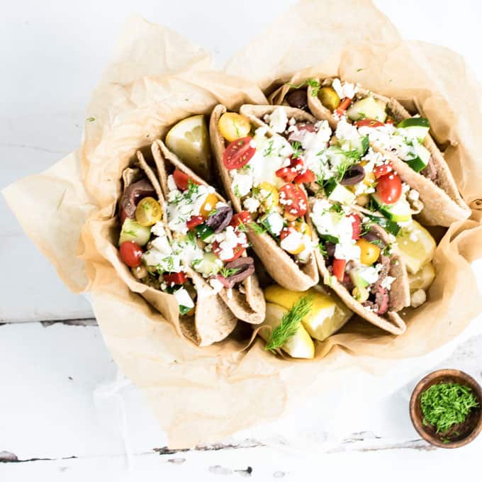 A bowl filled with Pitas and Steak, tomatoes, and lemons