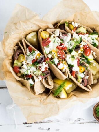 A bowl filled with Pitas and Steak, tomatoes, and lemons