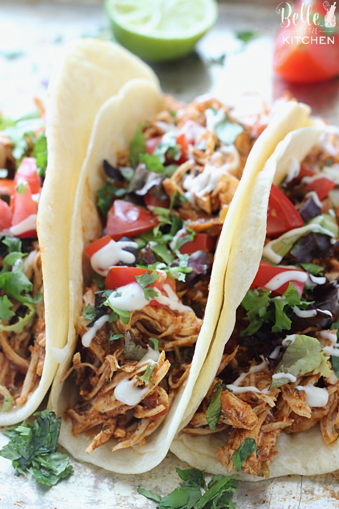 A plate of chicken tacos with tomatoes, lettuce, and sour cream drizzled on top