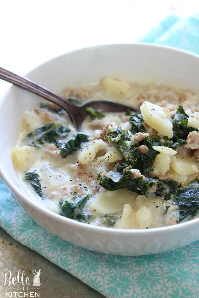 A bowl of soup with potatoes, kale, and sausage with a spoon