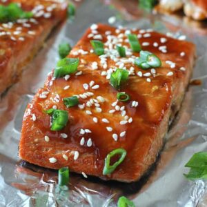 A close up of salmon with a glaze, sesame seeds, and green onions on top