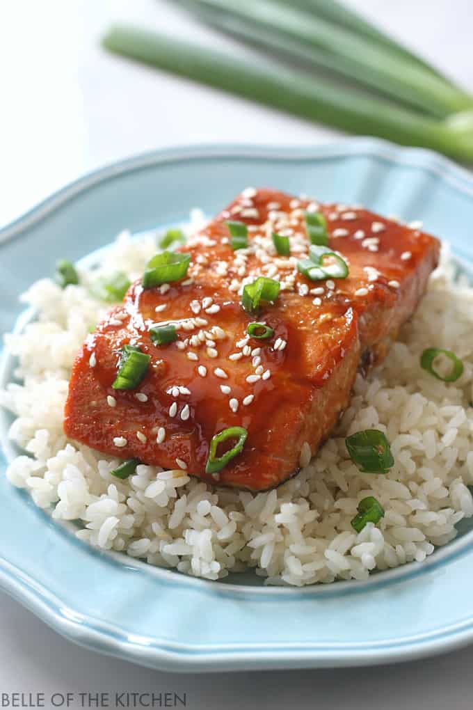 A close up of salmon with a glaze, sesame seeds, and green onions on top of rice