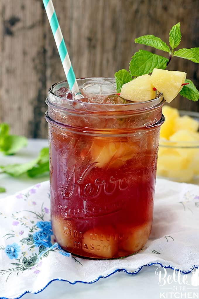 A glass of tea on a table in a mason jar with pineapple and mint