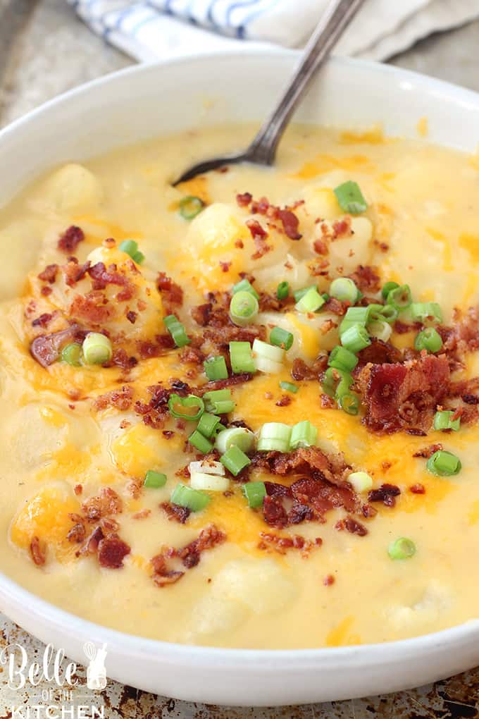 A bowl of potato soup with a spoon topped with bacon, cheese, and green onions